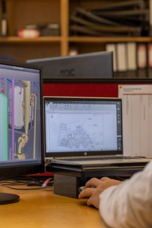 Engineer working with CAD software on dual monitors in an office setting.