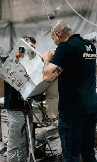 Two workers manage a control panel in an industrial setting, collaborating on machinery.